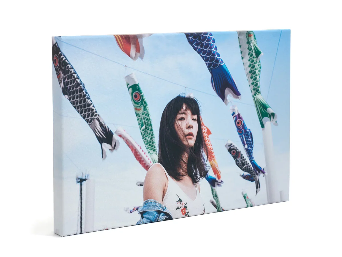 A painting on canvas shows a woman in front of a blue sky, surrounded by colorful, fish-shaped wind chimes suspended from ropes.