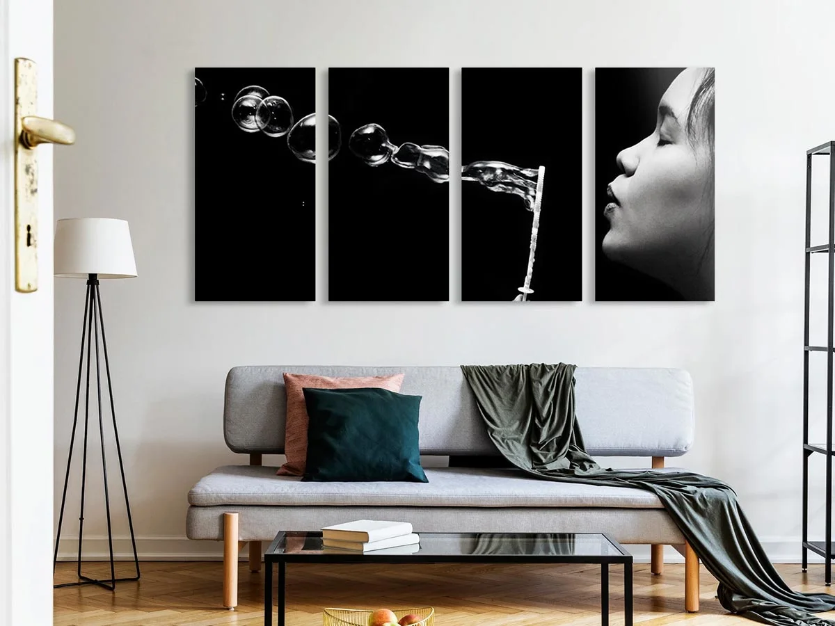 Multi-part picture with four black and white panels showing a woman breathing out soap bubbles. Panels are mounted on the wall above a sofa.