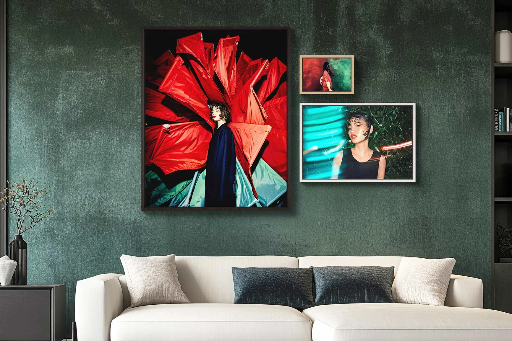 Ein Wohnzimmer mit einem weißen Sofa und drei gerahmten Fotografien an der Wand, darunter ein großes Porträt einer Person vor rotem Hintergrund.
