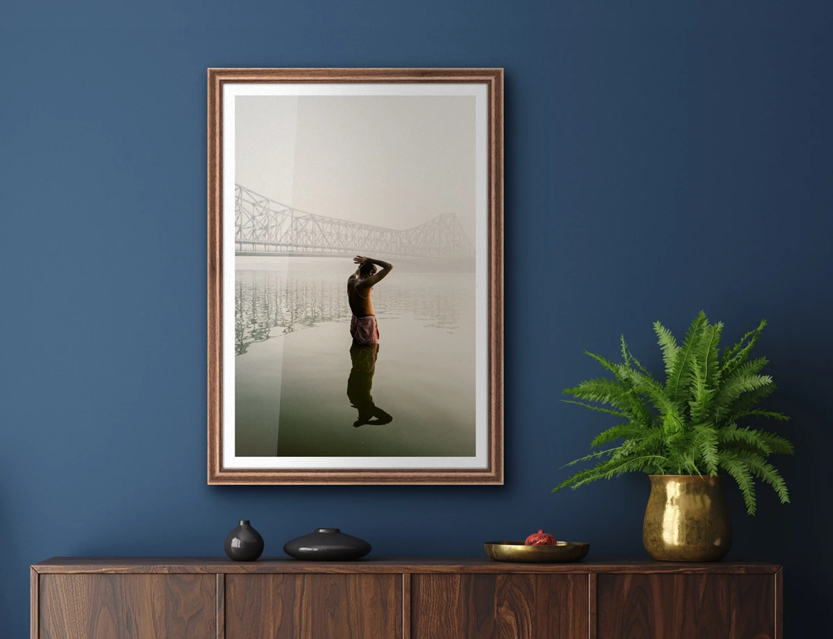 person standing in water with a bridge in the background as a framed print hanging on a wall.