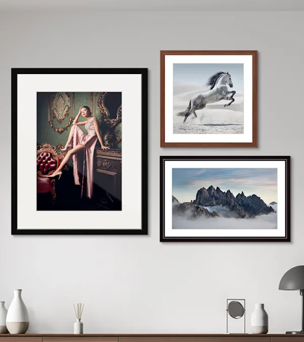Three framed art prints on gray wall: fashion portrait, leaping white horse, and misty mountain peaks.