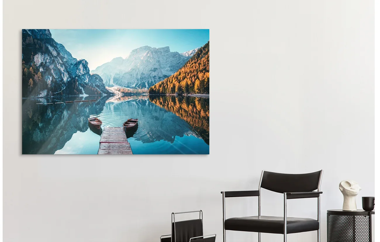 An acrylic print of a lake with mountains around it hangs on a wall.