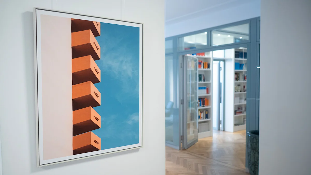 A framed photo of an orange building against a blue sky hangs on a white office wall, with a library room visible in the background.