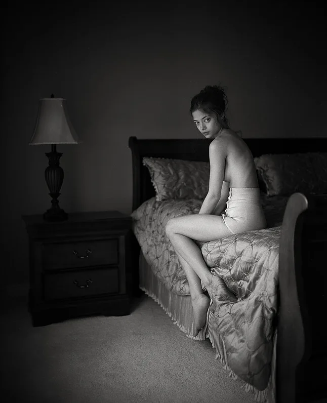 Woman sitting on a bed in lingerie and turning to the camera.