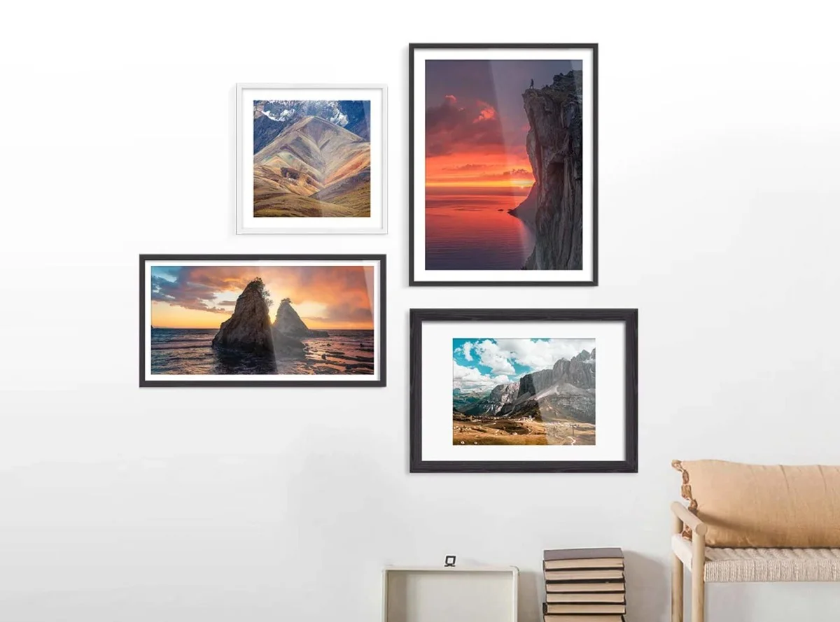 Vier Bilderrahmen mit Landschaftsfotografien an einer Wand. Zwei Bilder sind in weißen Rahmen, zwei in schwarzen.