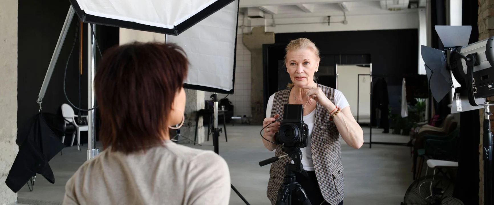 A photo studio with two people: one is standing behind a camera on a tripod, and the other is standing in front of it.