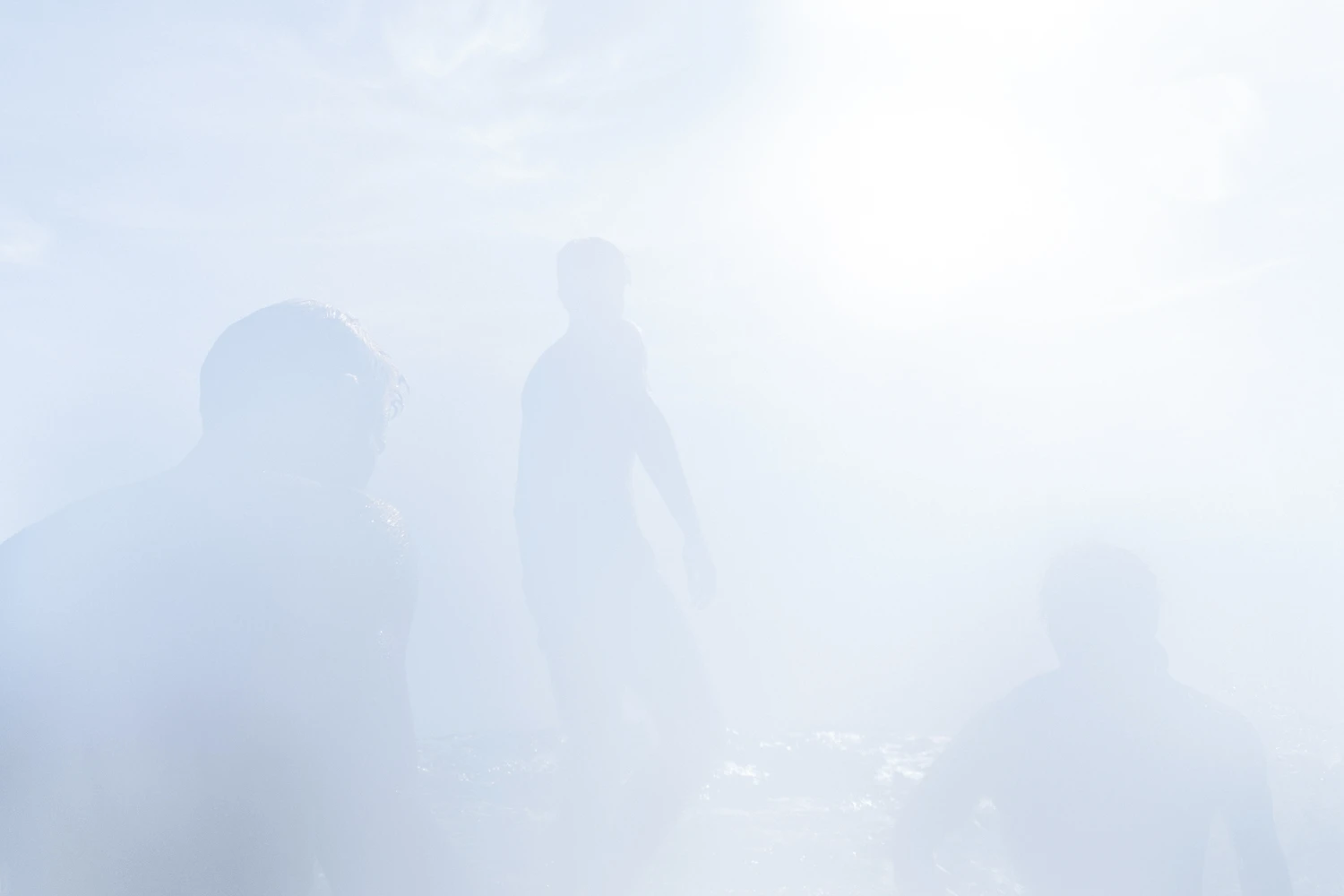 several young men stand on the edge of a cliff with the sun dazzling the lens