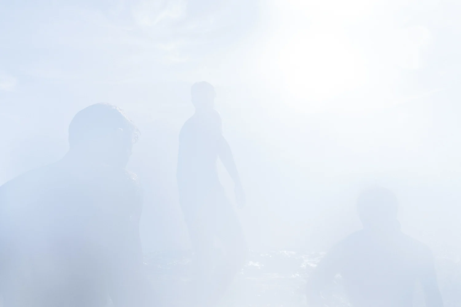 several young men stand on the edge of a cliff with the sun dazzling the lens