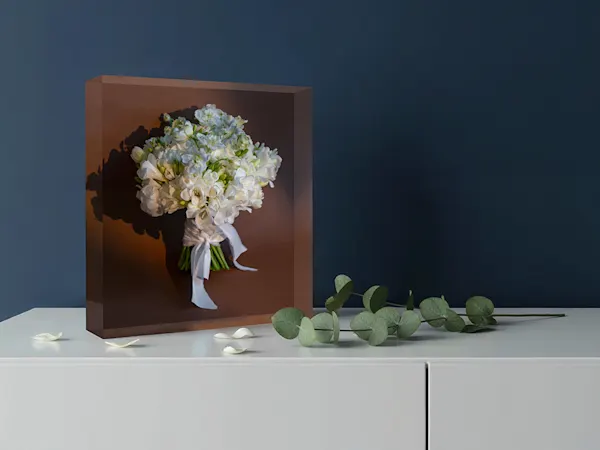 A square acrylic photo block displaying a white floral bouquet, placed on a white surface with eucalyptus sprigs nearby.