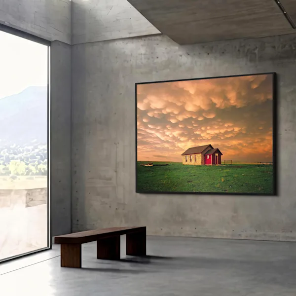 Una estancia moderna con paredes de hormigón, un banco de madera y un cuadro enmarcado en el que se ve una cabaña en un campo verde bajo un cielo espectacular.
