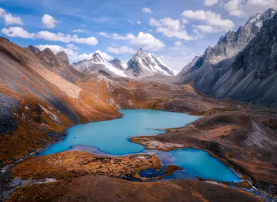 Ein türkisfarbener Bergsee zwischen schneebedeckten Bergen und felsigen Hängen unter einem blauen Himmel.