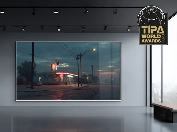 Photographie encadrée d'une station-service au crépuscule avec des lumières néon rouges, exposée dans un espace de galerie moderne avec le logo TIPA World Awards