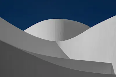 Architecture with curved, white walls against a blue sky.