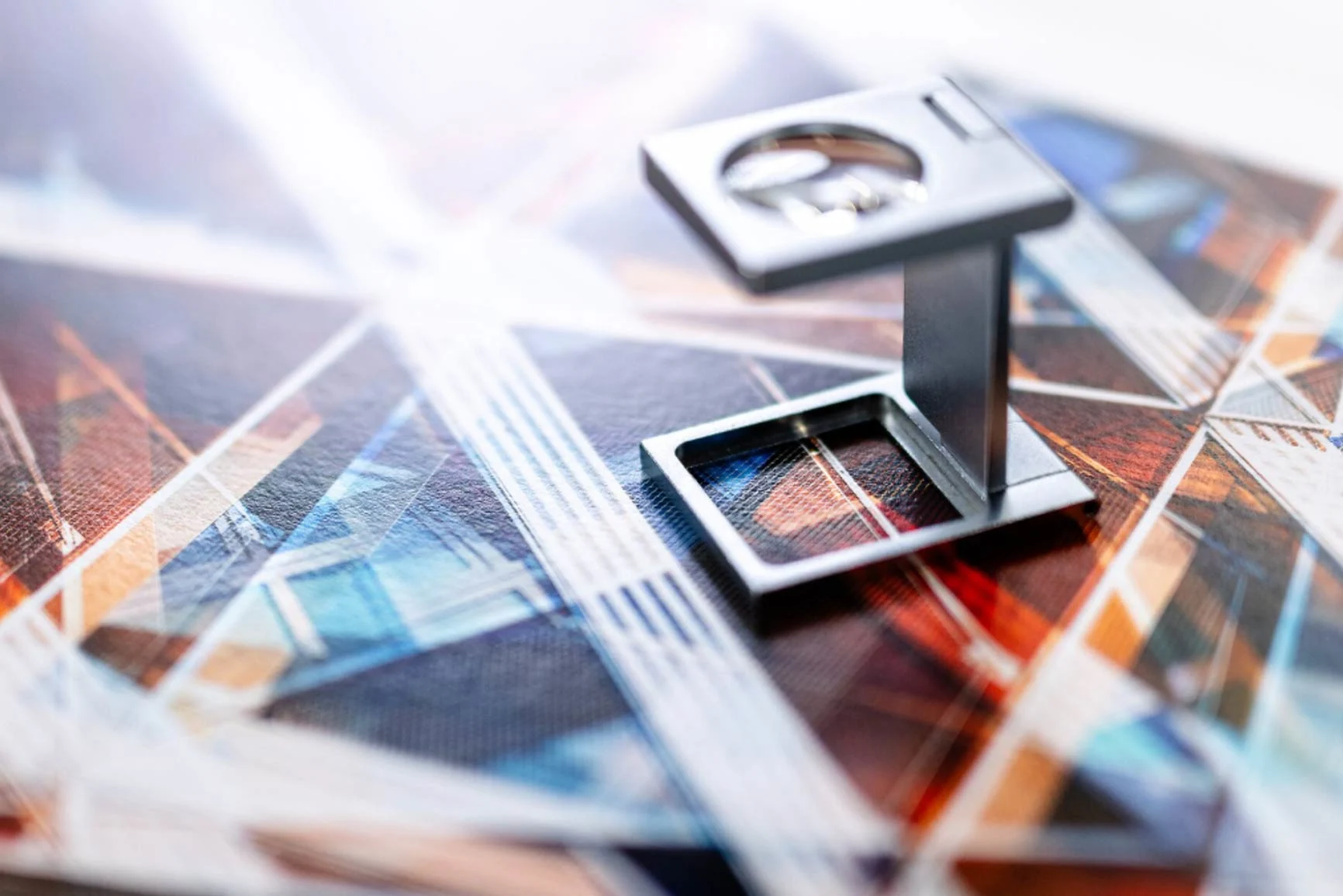 Metallische Lupe mit rechteckigem Ständer auf farbigem, geometrischem Muster.