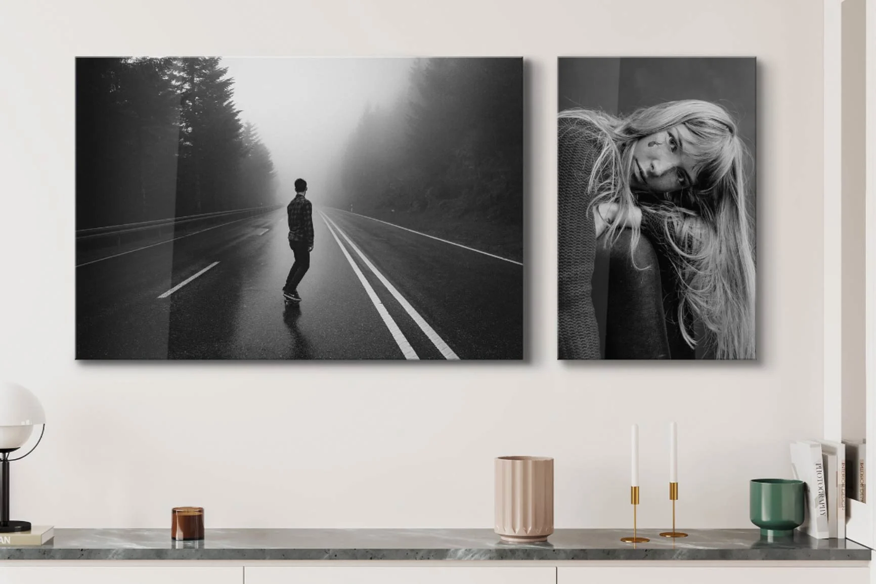 Due fotografie in bianco e nero su una parete bianca sopra un ripiano in marmo con candele e vasi.