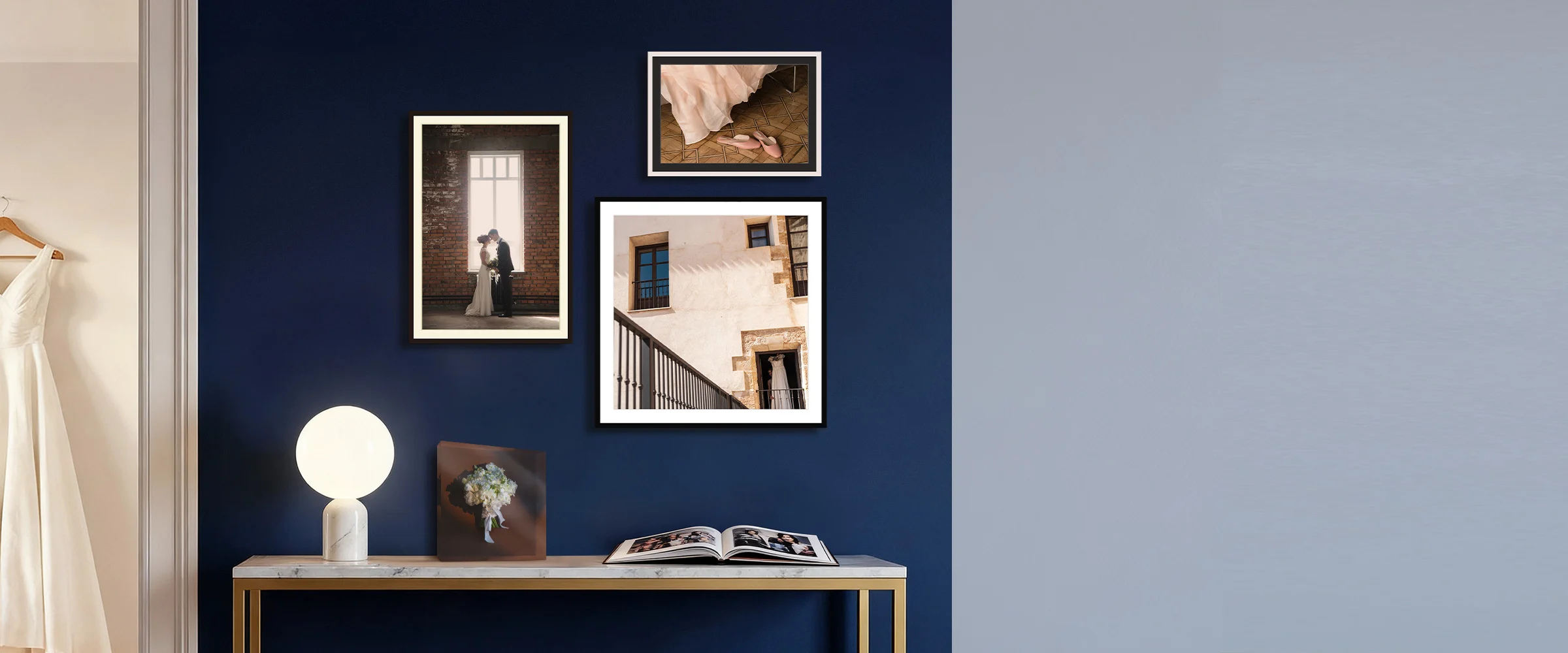 Three framed wedding photos on a navy wall above a marble console table and an open coffee table book.