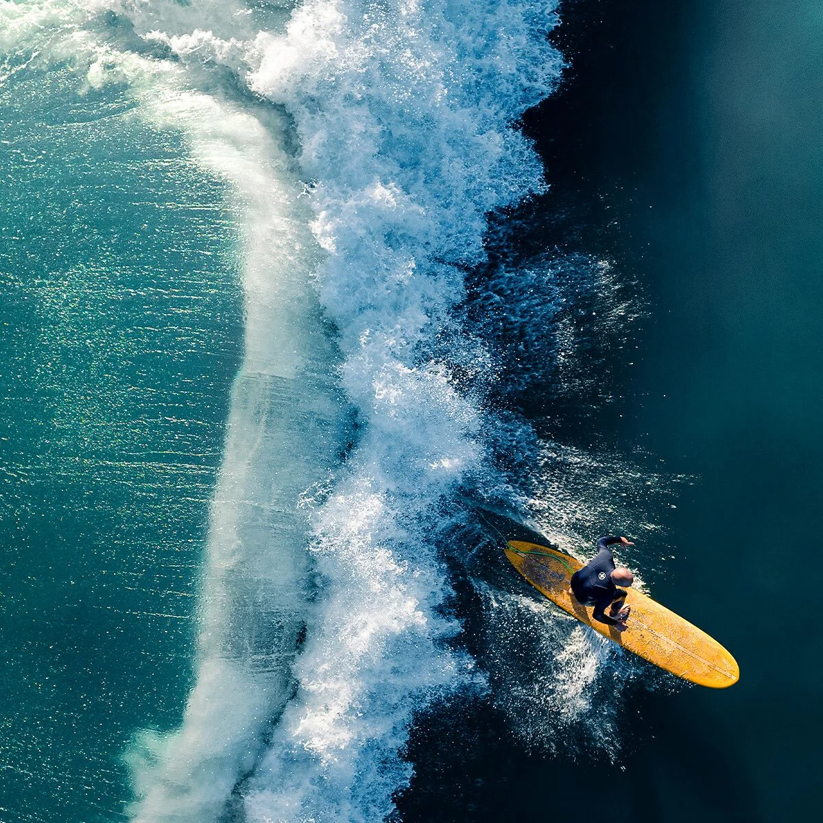 Surfer on yellow board riding a large wave breaking in the blue sea, aerial view.