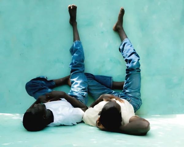 2 men lie on the ground against a wall, raising their legs in the air