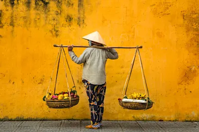 man holding a rack with 2 fruit baskets in front of a yellow wall.