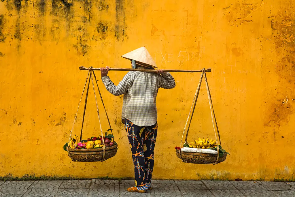 man holding a rack with 2 fruit baskets in front of a yellow wall.