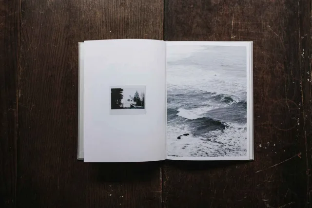 An open book with black and white photographs. On the left is a small photo, on the right a large photo of waves in the sea. Background made of dark wood.