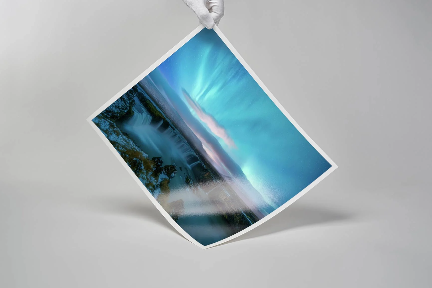Hand mit weißem Handschuh hält Fine Art Print mit Landschaftsmotiv, blauem Himmel und Wasserfall.