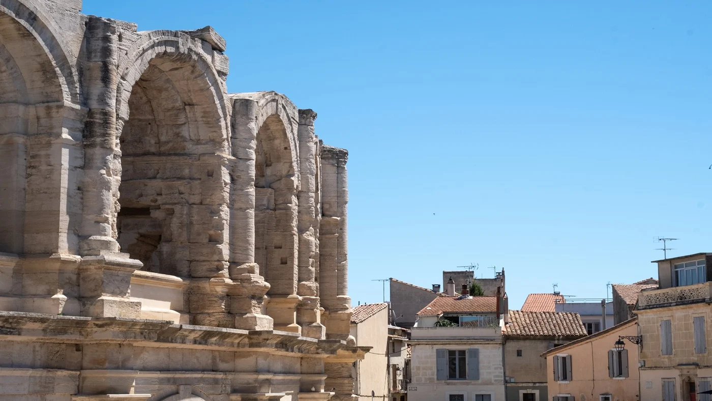view of the arles amphitheater. The sky is blue and on the right we can see a few houses in the city center.