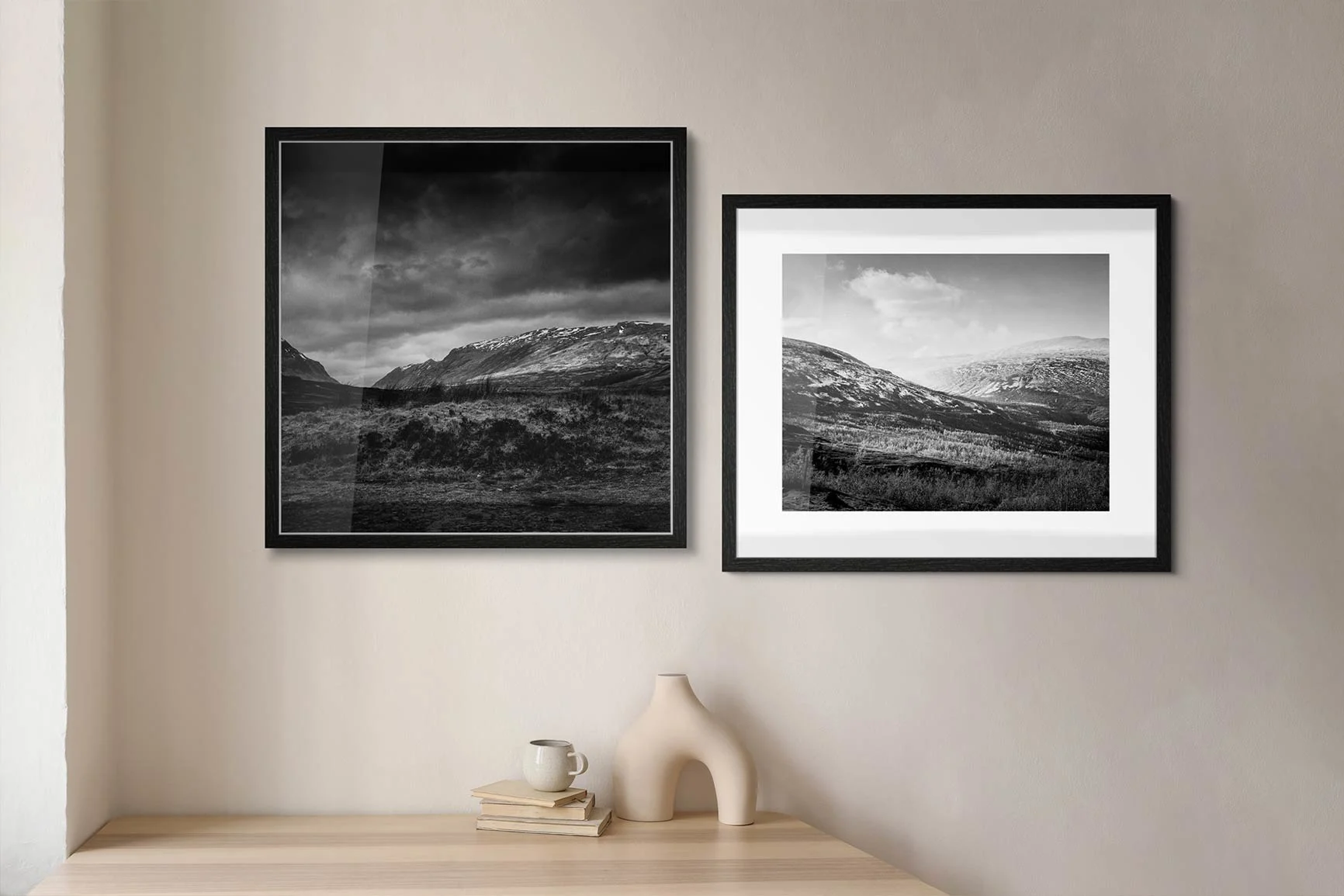 Due fotografie paesaggistiche in bianco e nero incorniciate sono appese a una parete chiara sopra una mensola di legno.