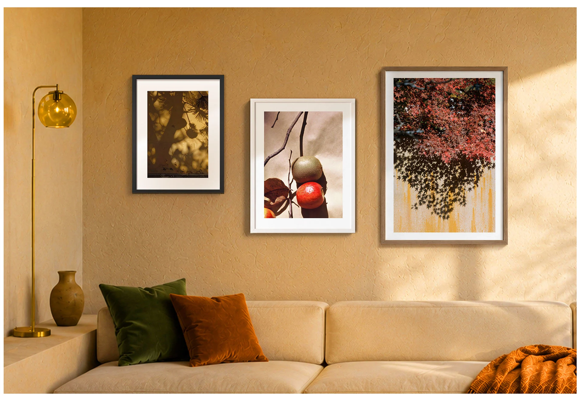 Drei gerahmte Fotografien mit Naturmotiven an einer warmen beigefarbenen Wand über einem cremefarbenen Sofa mit grünen und rostfarbenen Kissen sowie einer goldfarbenen Stehlampe.
