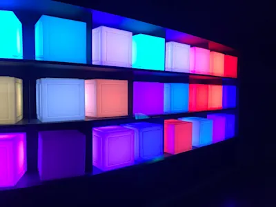 Leuchtende Würfel in Blau, Lila, Rosa und Rot in einem dunklen Regal.