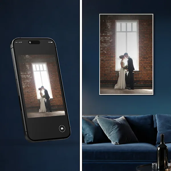 A phone displaying a wedding photo beside the same image printed and hung above a blue sofa in a dark living room.