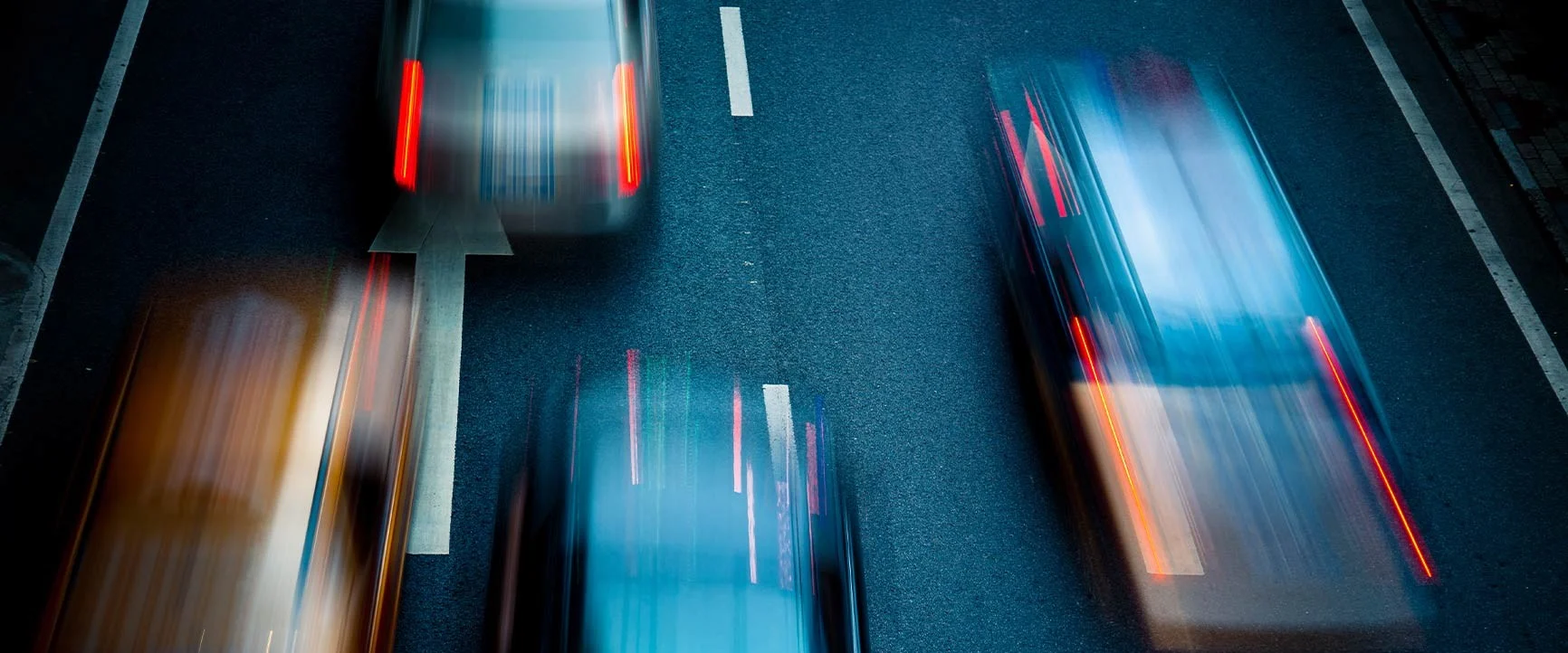 A bird's-eye view of a street with several moving, blurred vehicles.