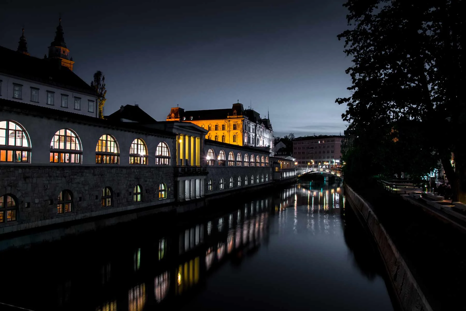 Illuminated historic buildings along a quiet river at night in a city.