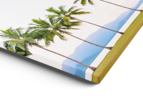 Une impression sur toile avec bordure miroir représentant des palmiers tropicaux sur fond de ciel bleu et d’océan, présentée en biais sur un fond blanc.