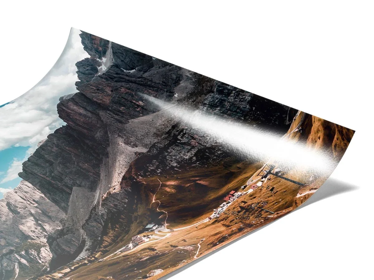 A picture on glossy photo paper shows a mountain landscape with blue skies and rocky cliffs. The photo paper is slightly curved.