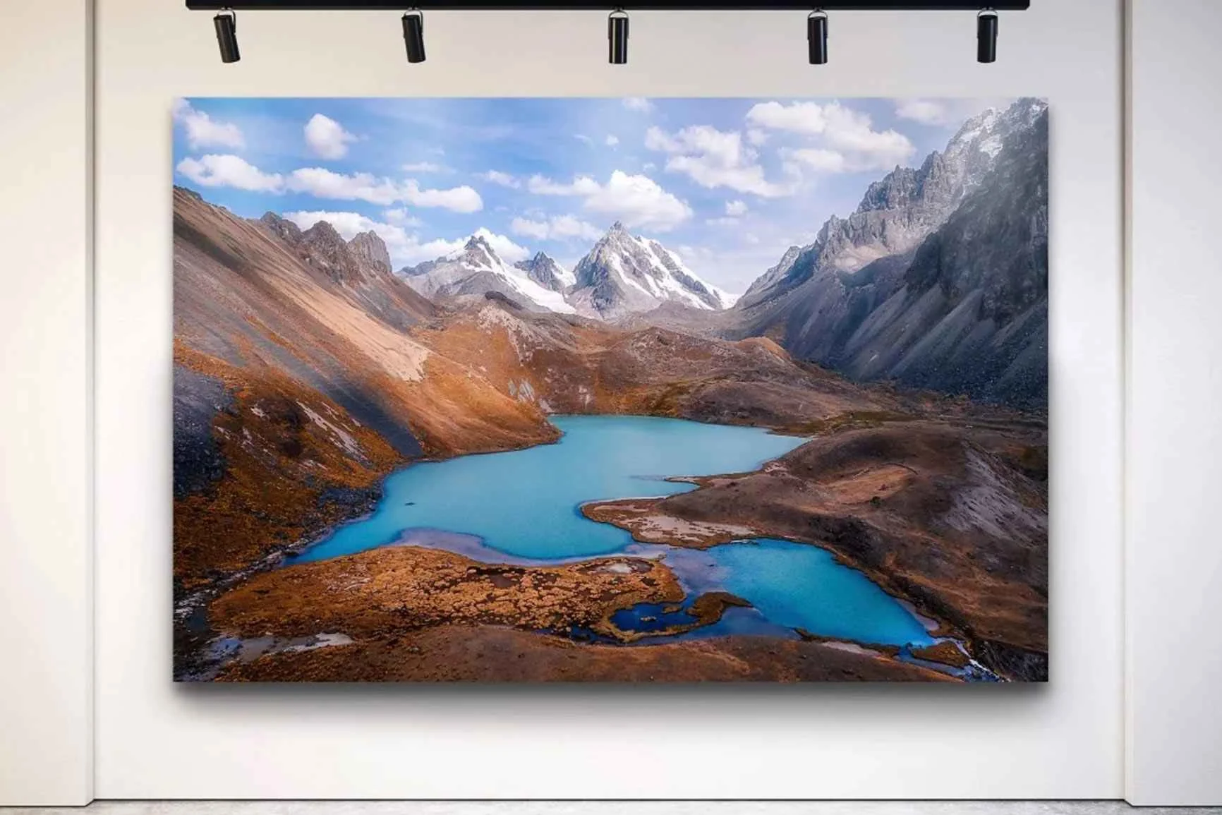 Stampa master di grande formato di WhiteWall su una parete bianca con panorama montano e lago blu sotto un cielo nuvoloso.