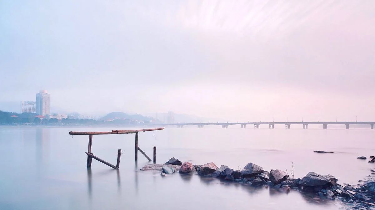 river and in the distance a bridge under a pinkish blue sky.