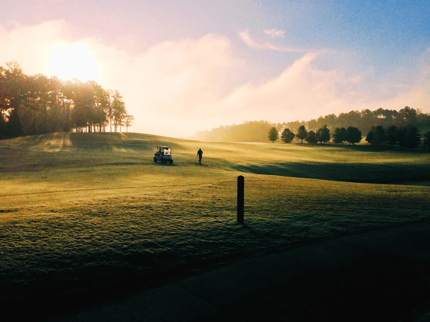 Golf course at sunrise with a golf cart and a person on the green.