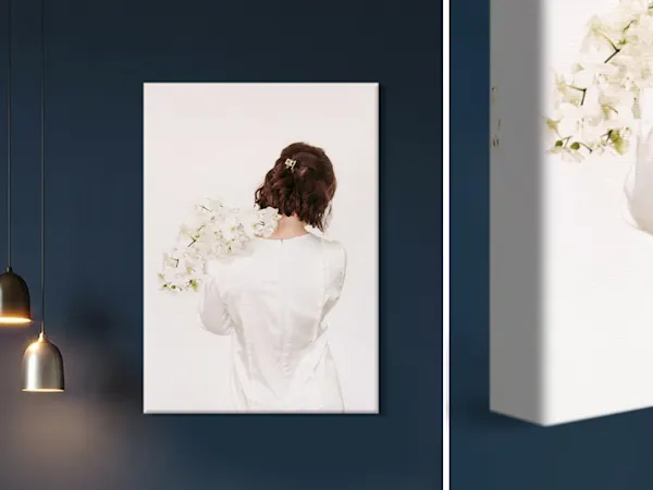 Canvas wall art showing a woman from behind in a white dress holding white flowers, displayed on a dark blue wall.
