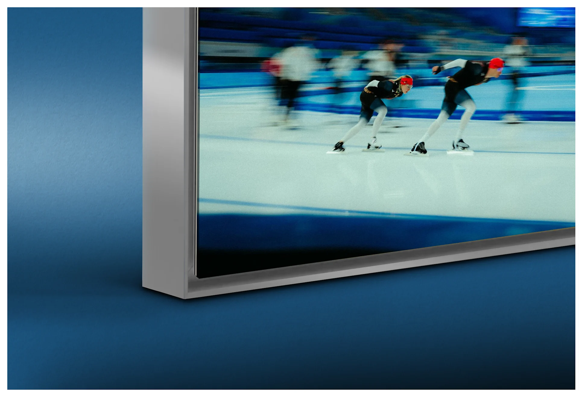 A close-up of the bottom-left corner of a high-quality silver aluminum Artbox frame. The framed image depicts speed skaters in action. A subtle shadow gap effect is visible between the print and the frame profile, providing a modern sense of depth.