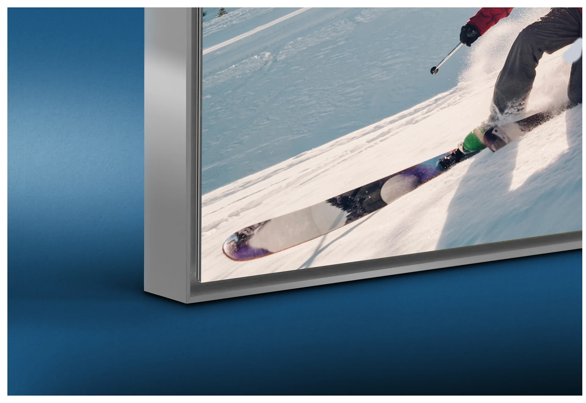 A close-up of the bottom-left corner of a high-quality silver aluminum Artbox frame. The framed image depicts speed skaters in action. A subtle shadow gap effect is visible between the print and the frame profile, providing a modern sense of depth.
