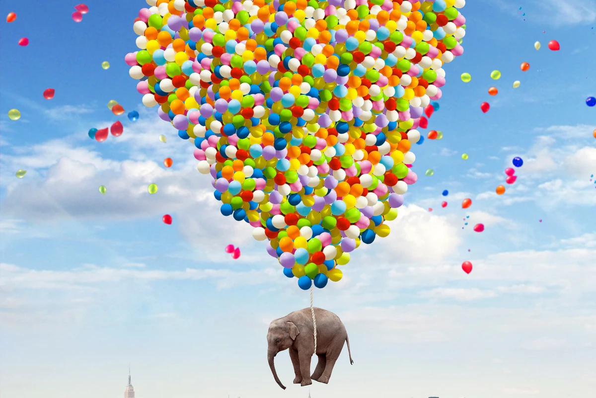 An elephant carried by thousands of colorful balloons above a city - photo by Robert Jahns.