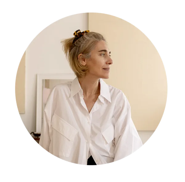 Una fotografia circolare del ritratto di Özlem Öszoy su uno sfondo chiaro, color crema. Guarda verso destra di profilo. Indossa una camicia bianca abbottonata e i suoi capelli biondi sono raccolti con un fermaglio a fantasia.