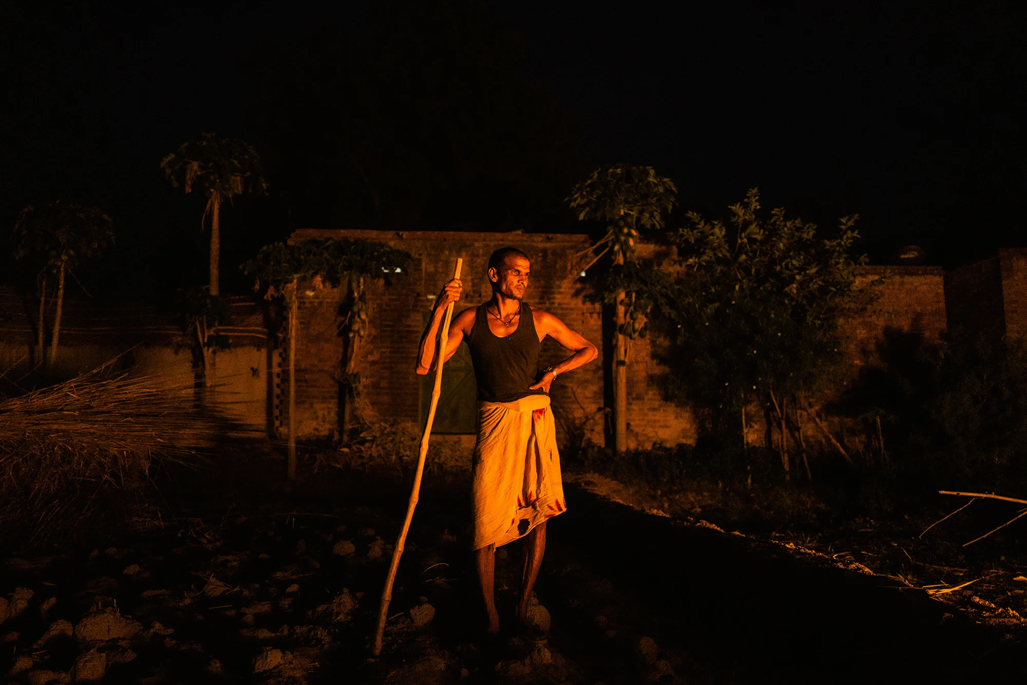 man with a wooden stick facing a light source.