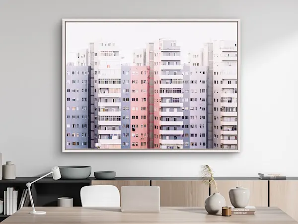 Impression sur toile dans un cadre flottant représentant des immeubles d’appartements rose pastel et bleu, accrochée au-dessus d’un bureau moderne avec un ordinateur portable, une lampe et des vases en céramique.