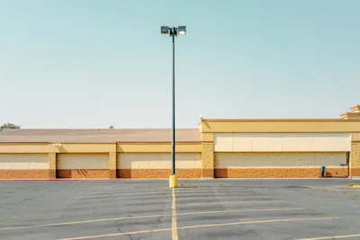 Lamppost on an empty parking lot in front of a flat building with beige-yellow walls and a clear sky.