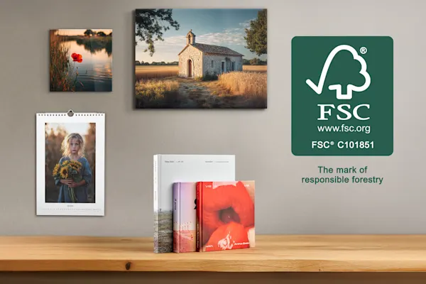 Various printed products, including wall art, a calendar, and photo books, are arranged on a wooden table and wall. To the right, the green FSC logo is displayed with the text "The mark of responsible forestry," indicating sustainable forest management.