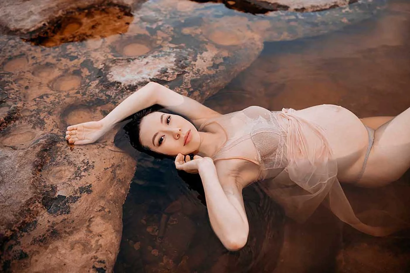 Pregnant woman lying in pool of water in stone landscape.