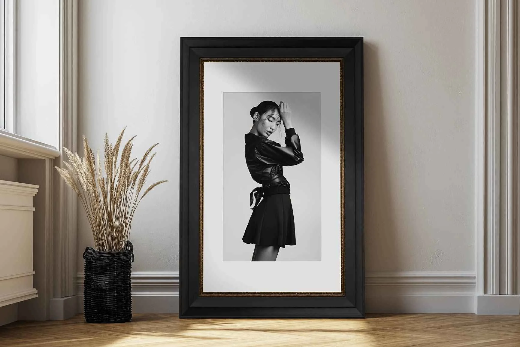 Schwarz-weiße Fotografie einer Frau in einem Kleid mit langärmligem Oberteil, gerahmt und auf einem Holzboden vor einer weißen Wand platziert