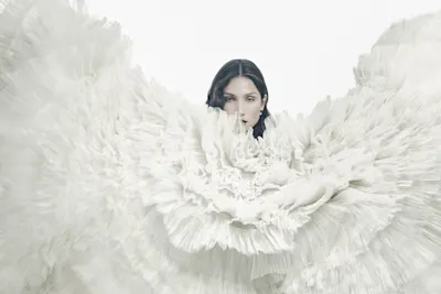 Fashion portrait surrounded by dramatic white feathers in a swirling pattern against light background